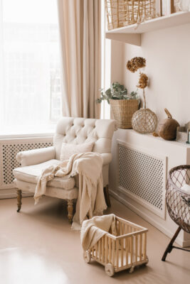 The living room is decorated in beige tones. A chair with a blanket and decor on the shelves in the house
